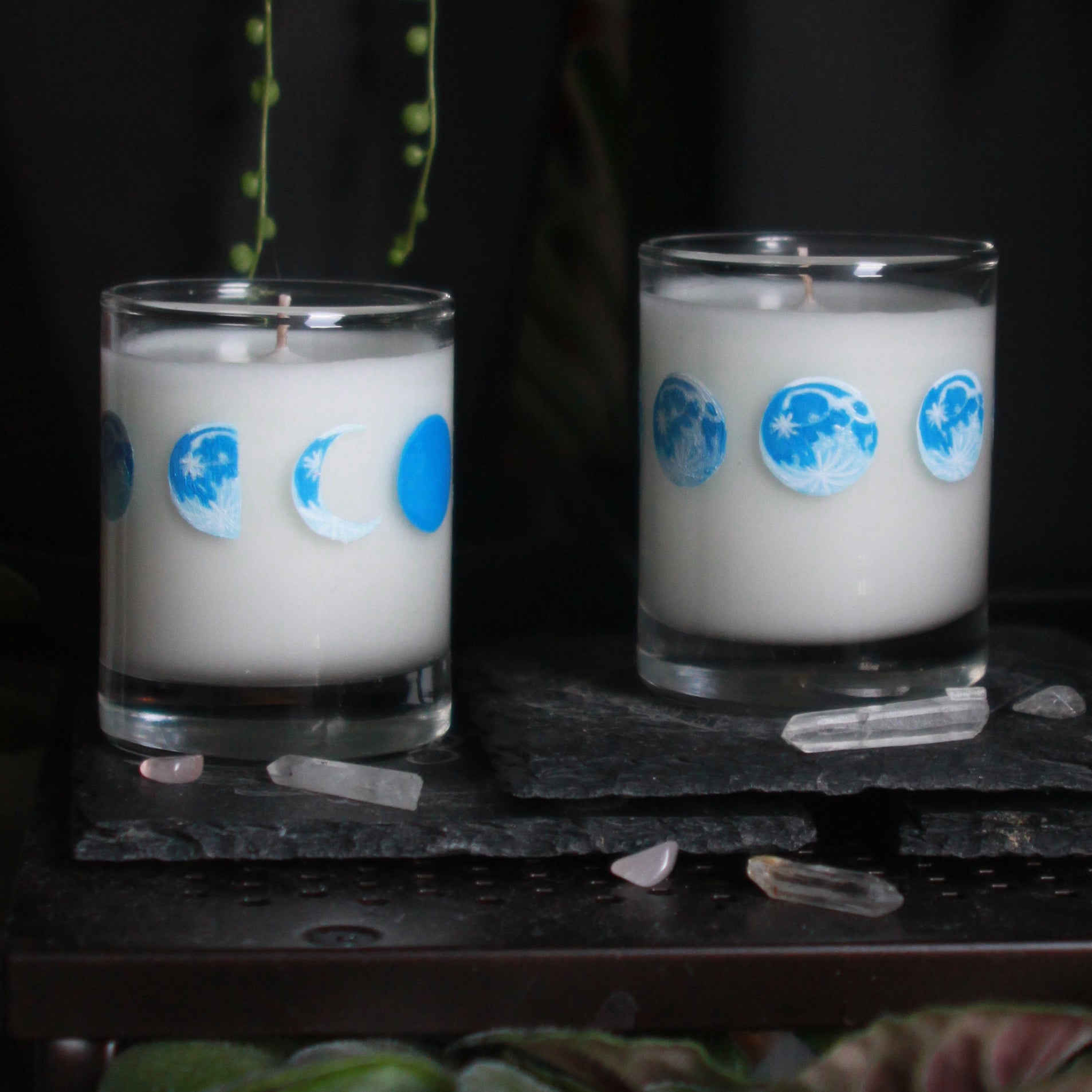 Three candle votives poured with white coconut-apricot wax each feature 8 hand-painted phases of the moon in shades of blue. The designs wraps around each glass.
